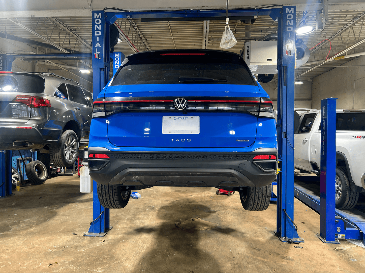 Blue Volkswagen Taos SUV elevated on a hydraulic lift inside a professional automotive repair garage.